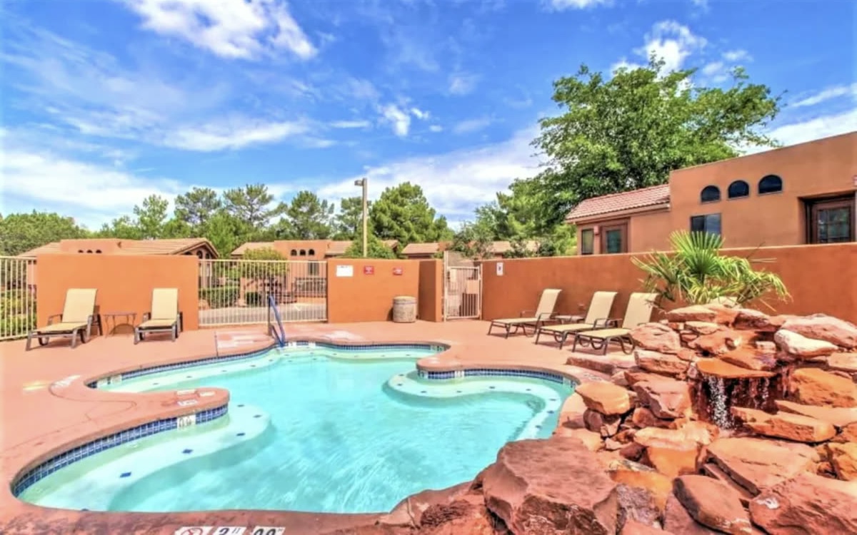 The Sedona Pines pool with a red rock waterfall feature and loungers under a blue sky